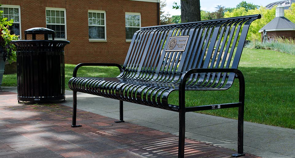 Midtown Bench with Back and inset Plaque and Litter Receptacle on a college campus